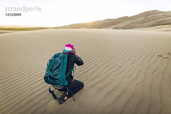 Wanderer in voller Länge mit Rucksack beim Kniend-Fotografieren im Great Sand Dunes National Park