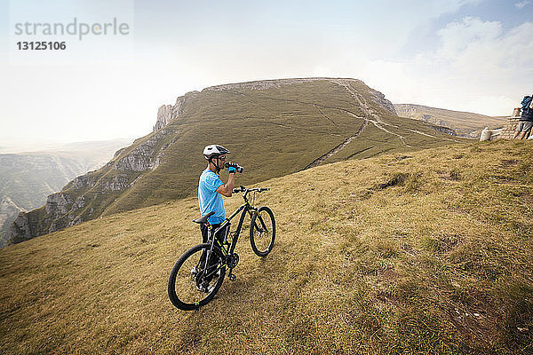 Seitenansicht eines Radfahrers  der Trinkwasser trinkt  während er auf einem Berg steht