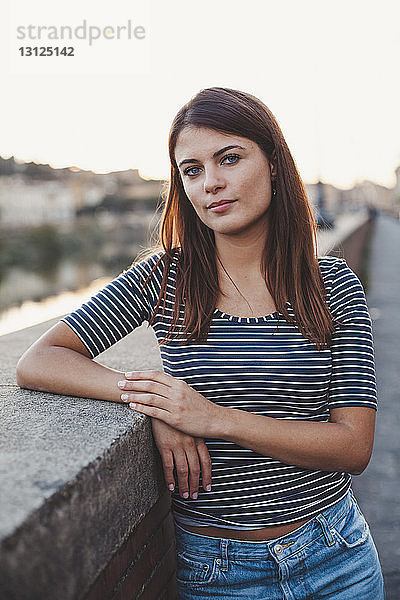 Porträt einer selbstbewussten jungen Frau  die an einer Stützmauer in der Stadt steht
