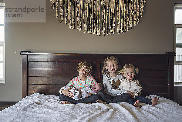 Porträt von lächelnden Schwestern mit einem kleinen Mädchen  das zu Hause auf dem Bett sitzt