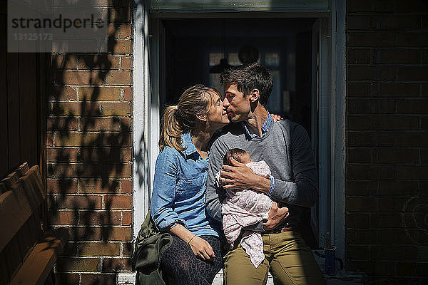 Paar mit küssendem Baby  das an der Tür sitzt
