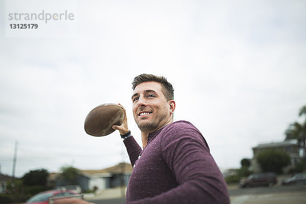 Lächelnder Mann wirft Fußball  während er gegen den Himmel steht