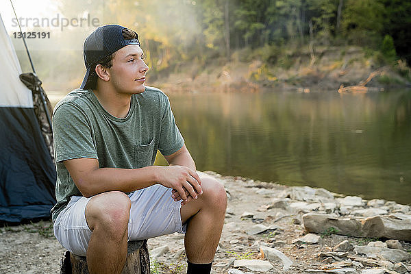 Junger Mann schaut weg  während er am See auf dem Campingplatz sitzt