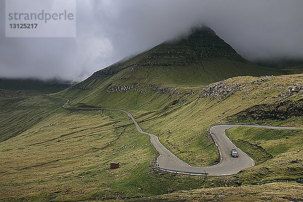 Hochwinkelaufnahme eines Autos auf kurvenreicher Straße gegen stürmische Wolken