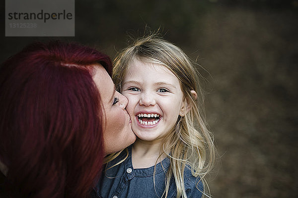 Porträt einer fröhlichen Tochter mit einer Mutter  die sie küsst