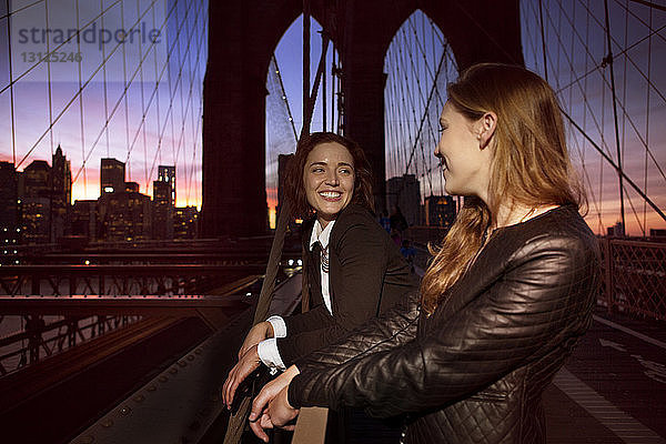 Fröhliche Freunde schauen sich an  während sie auf der Brooklyn Bridge stehen