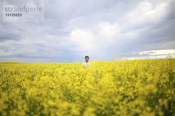 Mittelstrecke eines Mannes auf einem Rapsfeld gegen bewölkten Himmel