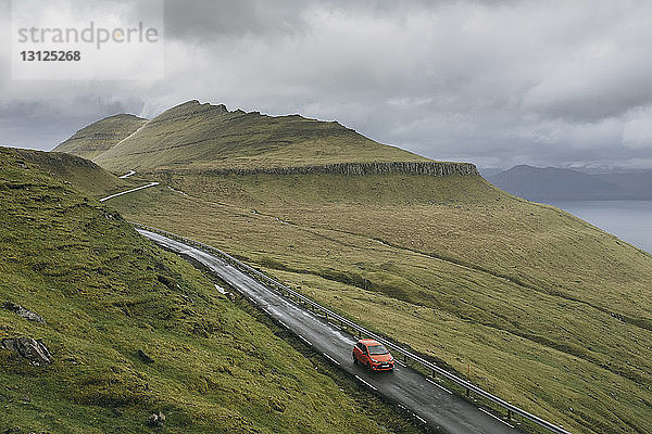 Hochwinkelaufnahme eines Autos auf einer Bergstraße vor stürmischen Wolken