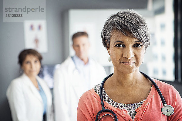 Porträt einer selbstbewussten Ärztin in der Klinik mit im Hintergrund stehenden Kollegen