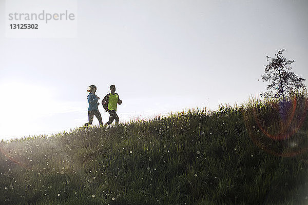Männliche und weibliche Athleten laufen bei Sonnenuntergang auf Grasfeld