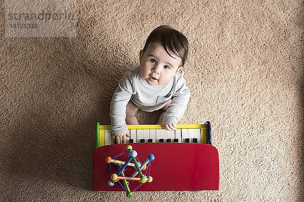 Portrait eines süßen kleinen Jungen  der zu Hause auf einem Teppich Spielzeugklavier spielt