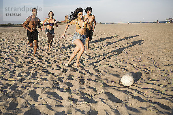 Glückliche Freunde spielen an sonnigen Tagen Fussball am Strand