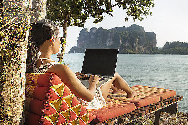 Frau benutzt Laptop-Computer  während sie auf Liegestuhl gegen das Meer sitzt