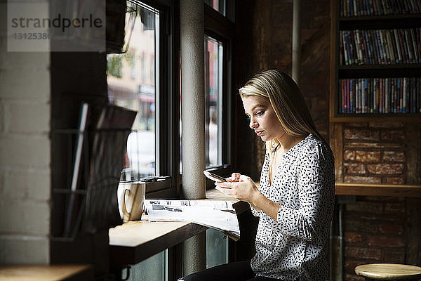 Junge Frau telefoniert beim Zeitungslesen am Tisch im Café
