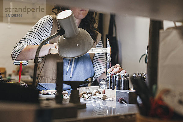 Mitschnitt einer Handwerkerin  die mit Handwerkzeugen arbeitet  während sie in einer Werkstatt Schmuck auf dem Tisch herstellt