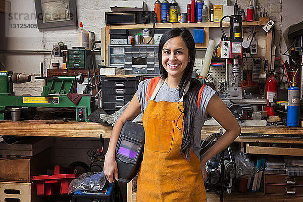 Porträt einer glücklichen Mechanikerin mit Schürze in der Werkstatt