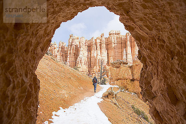 Rückansicht eines Bergwanderers  der im Winter durch den Höhleneingang des Bryce Canyon Nationalparks wandert