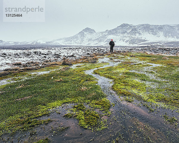 Mitteldistanzansicht eines Wanderers  der im Winter auf dem Feld vor schneebedeckten Bergen steht