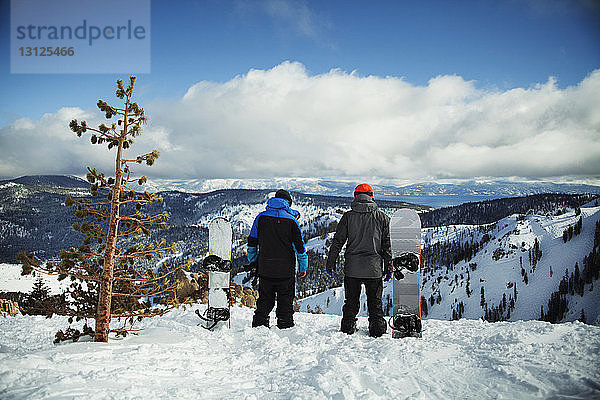 Freunde mit Snowboard stehen auf verschneitem Feld gegen den Himmel