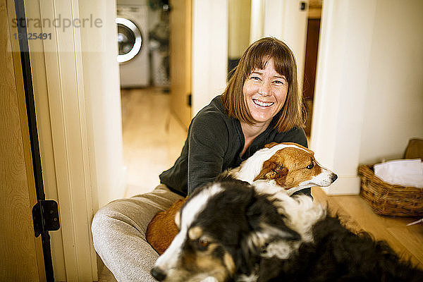 Porträt einer Frau mit Hunden  die zu Hause auf dem Boden sitzt