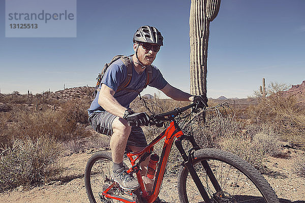 Selbstbewusster Mann fährt Mountainbike auf Landschaft gegen klaren blauen Himmel