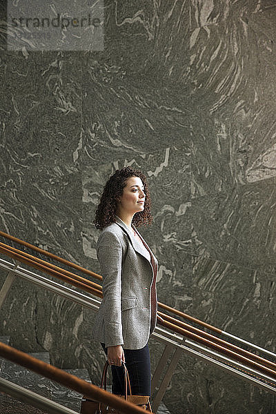 Seitenansicht einer nachdenklichen Geschäftsfrau  die auf Stufen in einem modernen Gebäude steht