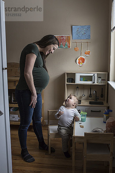 Lächelnde schwangere Mutter sieht Sohn beim Spielen mit Spielzeug an