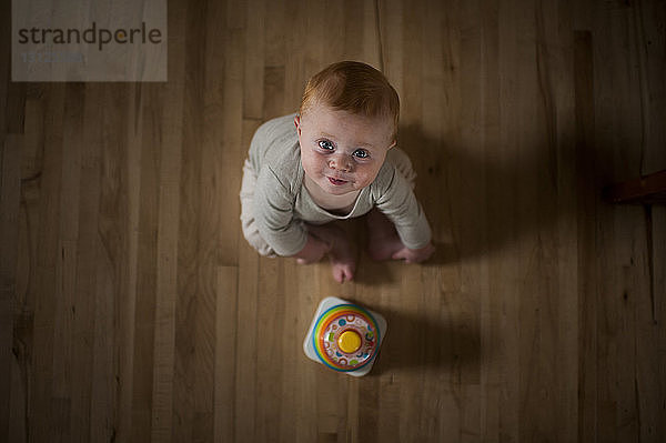 Portrait eines süßen kleinen Jungen mit Spielzeug  der zu Hause auf dem Boden sitzt
