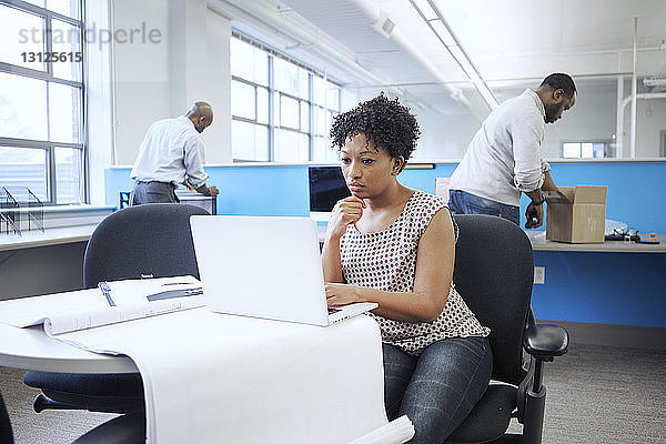 Geschäftsfrau benutzt Laptop-Computer  während männliche Kollegen im Hintergrund arbeiten