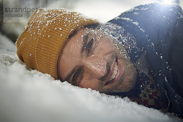 Porträt eines lächelnden Mannes  der sich bei Schneefall auf eine schneebedeckte Motorhaube stützt