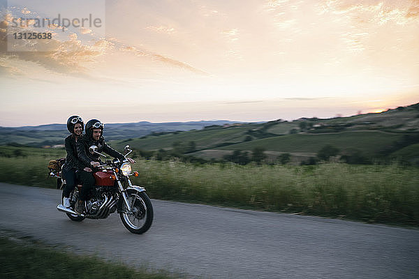 Junges Paar fährt bei Sonnenuntergang auf einem Motorrad auf der Landstraße