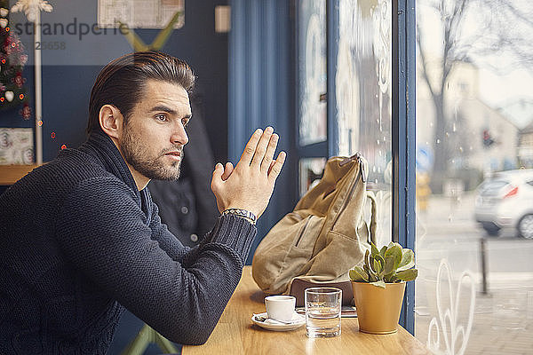 Seitenansicht eines Mannes  der durch ein Fenster schaut  während er im Café sitzt