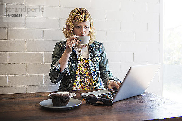 Frau trinkt Kaffee  während sie im Café einen Laptop benutzt