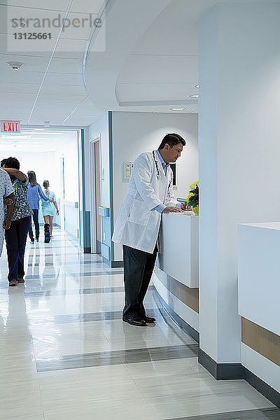 Arzt steht am Krankenhausempfang mit Kollegen und Patienten im Hintergrund