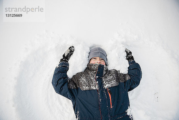 Draufsicht eines spielenden Jungen  der im Winter beim Spielen einen Schneeengel macht