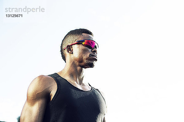Nachdenklicher männlicher Athlet mit Sonnenbrille bei klarem Himmel