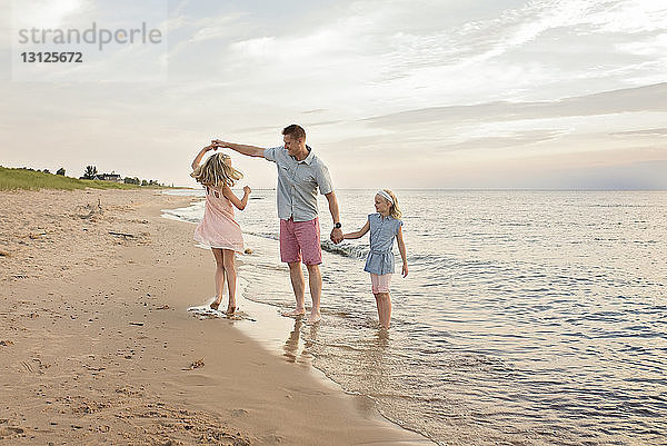 Vater spielt mit Töchtern am Strand am Ufer