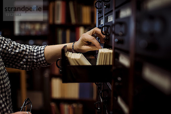 Geschnittene Hand einer Frau  die Bibliotheksausweise aus der Schublade nimmt