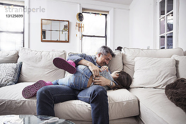 Fröhlicher Vater spielt mit Tochter zu Hause auf dem Sofa