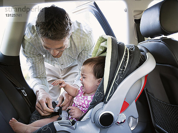 Baby weint  während der lächelnde Vater den Autositz verriegelt