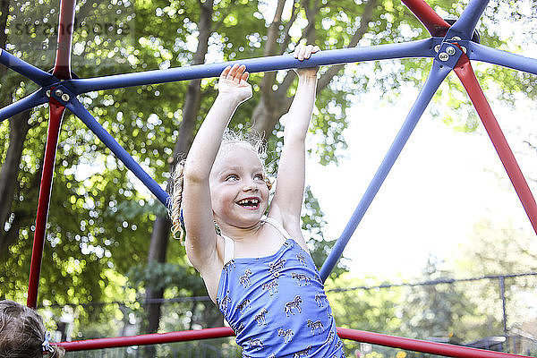 Fröhliches süßes Mädchen klettert auf dem Spielplatz im Dschungel gegen Bäume