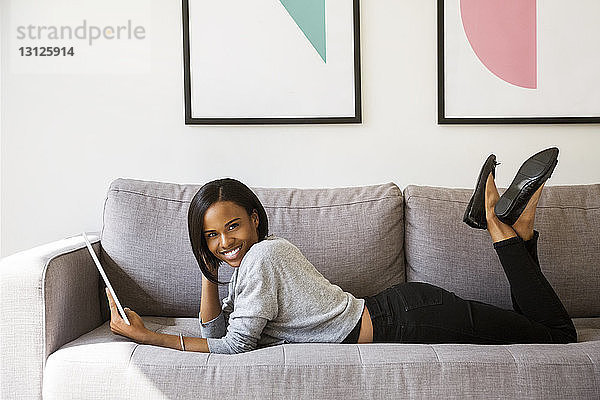 Seitenansicht Porträt einer glücklichen Frau  die einen Tablet-Computer hält  während sie zu Hause auf dem Sofa liegt