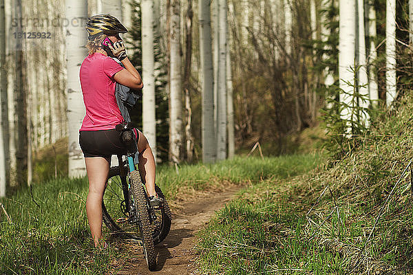 Sportlerin  die ein Mobiltelefon benutzt  während sie mit dem Fahrrad im Wald steht