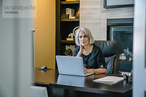 Porträt einer Geschäftsfrau  die am Laptop-Computer am Schreibtisch im Büro arbeitet  durch die Tür gesehen