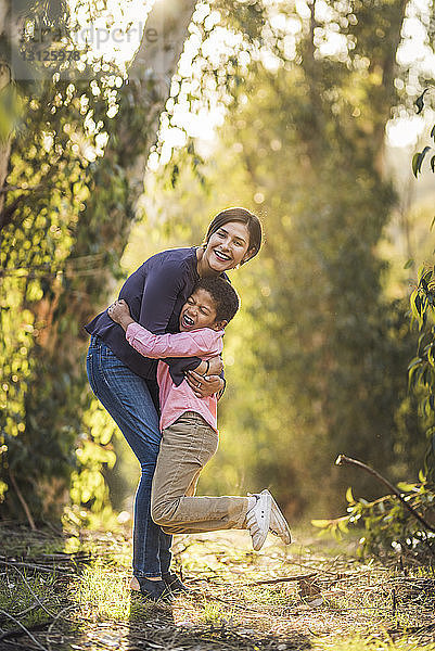 Bildnis einer fröhlichen Mutter  die ihren Sohn umarmt  während sie im Wald steht