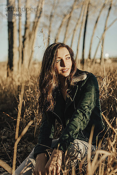 Lächelnde junge Frau schaut weg  während sie auf dem Feld sitzt