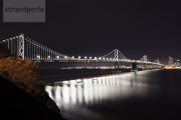 Beleuchtete Oakland Bay Bridge über dem Meer gegen den Himmel bei Nacht