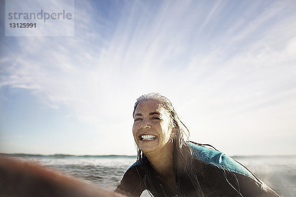 Fröhliche reife Frau surft im Meer gegen den Himmel