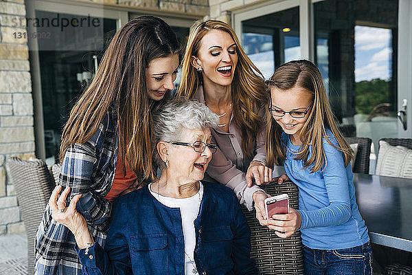 Mittlere erwachsene Frau  die mit Mutter und Töchtern auf der Veranda ein Smartphone benutzt