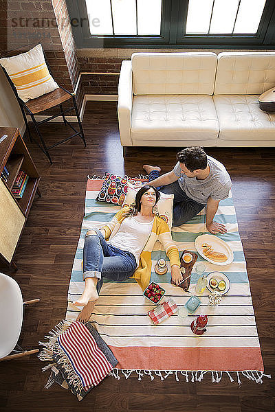 Hochwinkelansicht eines Paares  das sich beim Essen auf dem Teppich entspannt